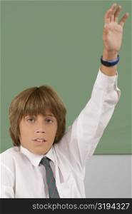 Portrait of a schoolboy with his hand raised in a classroom