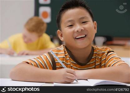 Portrait of a schoolboy writing on a notebook with a pencil and smiling