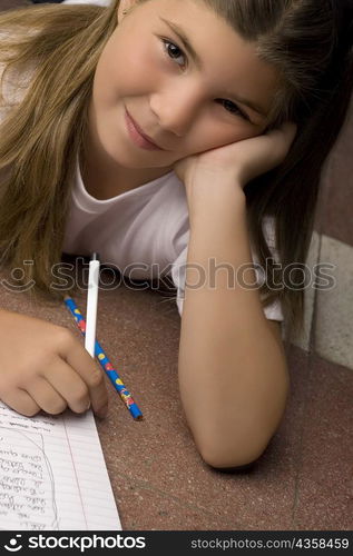 Portrait of a schoolgirl lying on the floor and writing on a textbook