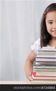 Portrait of a schoolgirl smiling with a stack of books in front of her
