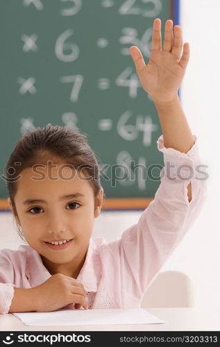 Portrait of a schoolgirl with her hand raised in a classroom