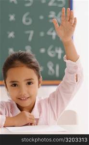 Portrait of a schoolgirl with her hand raised in a classroom