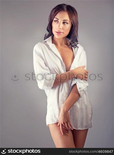 Portrait of a seductive woman wearing man's shirt posing over gray background, stunning female, sexy morning look