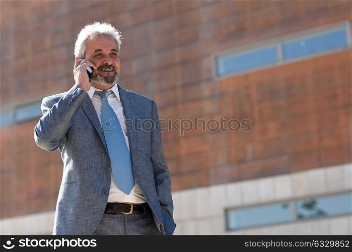 Portrait of a senior businessman talking with a smart phone outside of modern office building. Successful business man in urban background.