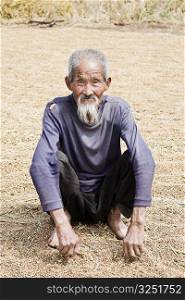 Portrait of a senior man crouching over rice grains, Zhigou, Shandong Province, China