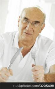 Portrait of a senior man holding a fork and a table knife