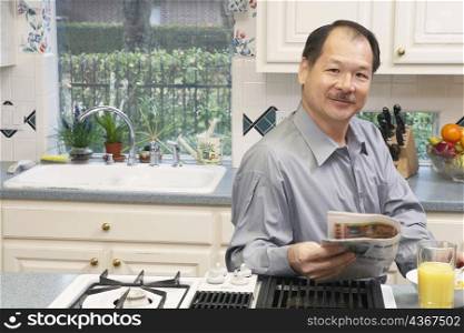 Portrait of a senior man holding a newspaper in the kitchen