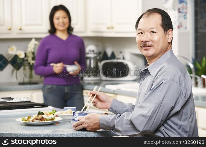 Portrait of a senior man holding a pair of chopsticks with a mature woman standing behind him