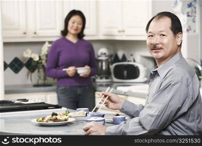 Portrait of a senior man holding a pair of chopsticks with a mature woman standing behind him