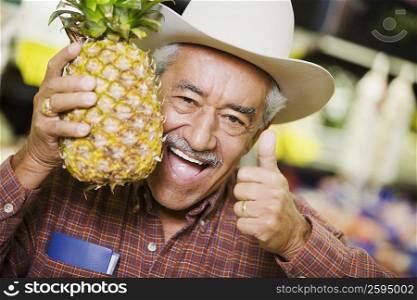 Portrait of a senior man holding a pineapple and showing a thumbs up sign
