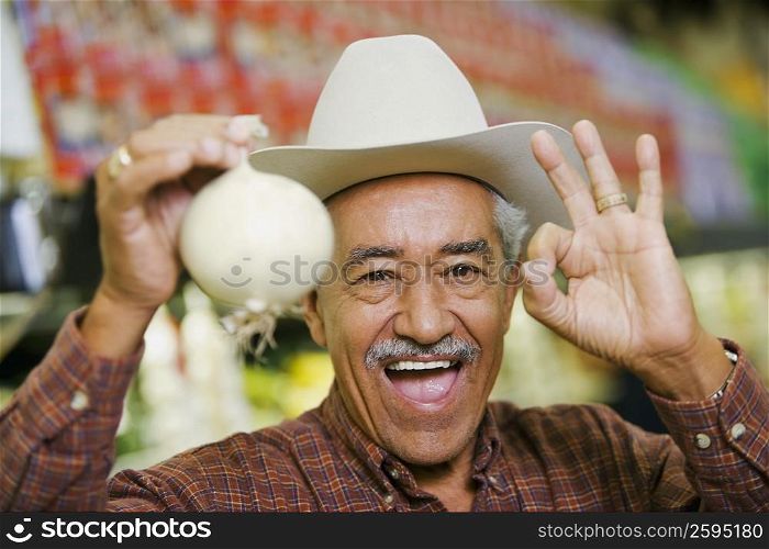 Portrait of a senior man holding a white onion and making an ok sign