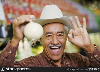 Portrait of a senior man holding a white onion and making an ok sign