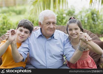 Portrait of a senior man holding his grandchildren&acute;s hands and smiling