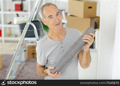 portrait of a senior man holding roll of wallpaper