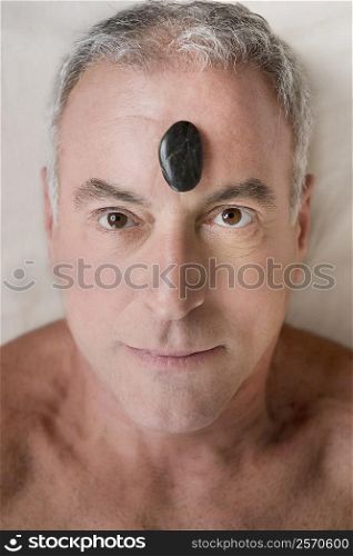 Portrait of a senior man lying on a massage table with a pebble on his forehead