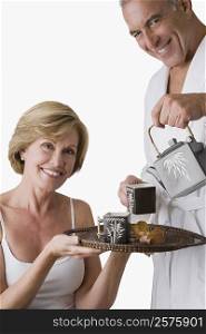 Portrait of a senior man pouring tea from a tea kettle into the cup with a mature woman holding a tray