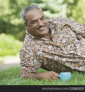 Portrait of a senior man reclining in a lawn and holding a tea cup