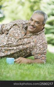 Portrait of a senior man reclining in a lawn and holding a tea cup
