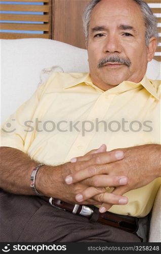 Portrait of a senior man sitting on a couch with his hands clasped