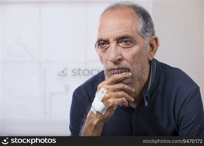 Portrait of a senior man sitting with a bandage on his hand. (Health and fitness)