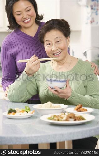 Portrait of a senior woman eating food with her daughter standing behind her