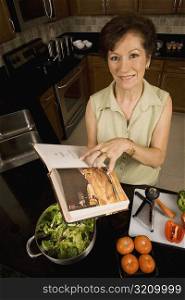 Portrait of a senior woman holding a cookbook in the kitchen and smiling