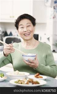 Portrait of a senior woman holding a pair of chopsticks and a bowl
