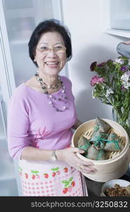 Portrait of a senior woman holding dumplings in a bamboo steamer
