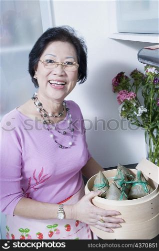 Portrait of a senior woman holding dumplings in a bamboo steamer
