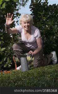 Portrait of a senior woman kneeling in a garden and waving her hand