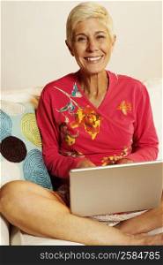 Portrait of a senior woman sitting on a couch and using a laptop