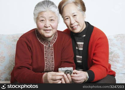 Portrait of a senior woman sitting on a couch with a mature woman holding a digital camera