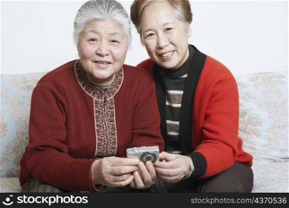 Portrait of a senior woman sitting on a couch with a mature woman holding a digital camera