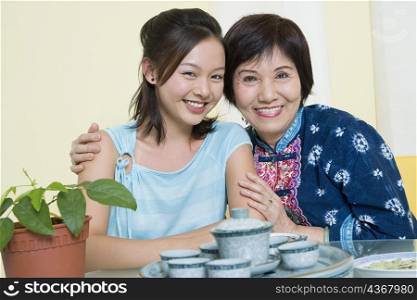 Portrait of a senior woman sitting with her arm around her granddaughter at a table and smiling