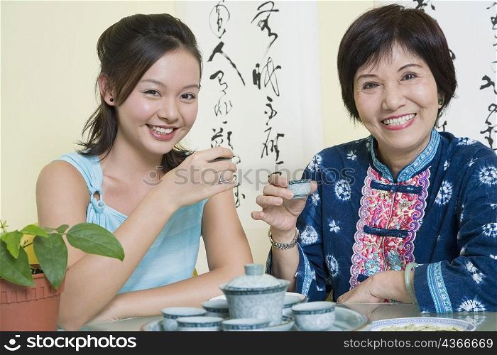 Portrait of a senior woman sitting with her granddaughter at a table and holding tea cups
