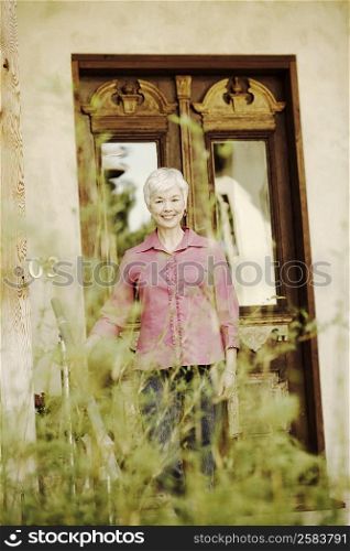 Portrait of a senior woman standing in front of a closed door and smiling