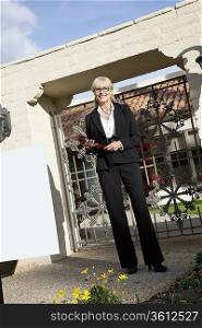 Portrait of a senior woman standing with clipboard in front of entrance gate
