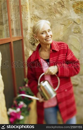 Portrait of a senior woman watering plants with watering can and smiling