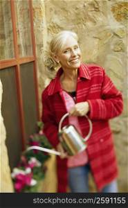 Portrait of a senior woman watering plants with watering can and smiling