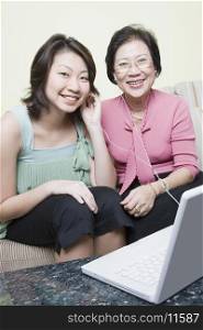 Portrait of a senior woman with her granddaughter sitting on a couch in front of a laptop