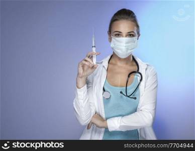 Portrait of a Serious Confident Doctor Woman with an Syringe isolated on Blue Background. Vaccination and Antiviral Injection Concept. Copy Space.. Doctor with an Injector