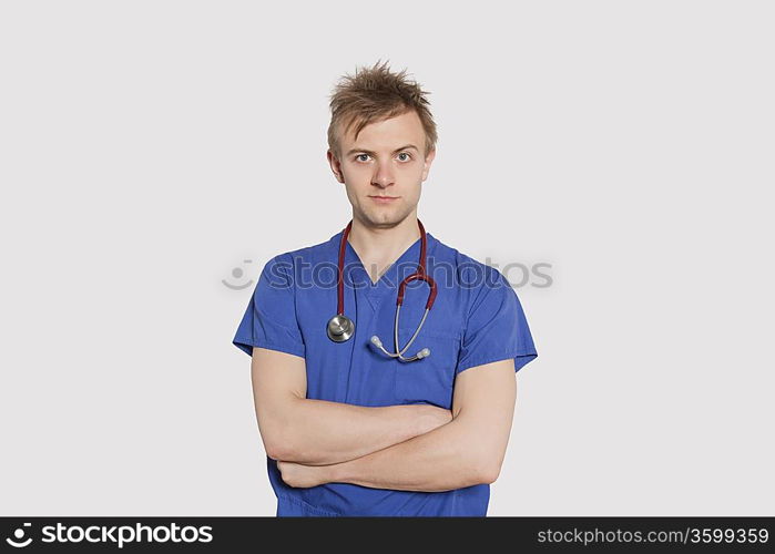 Portrait of a serious male surgeon standing with arms crossed over gray background