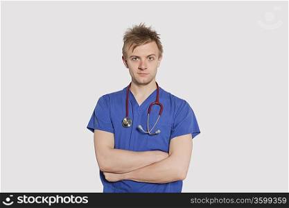 Portrait of a serious male surgeon standing with arms crossed over gray background