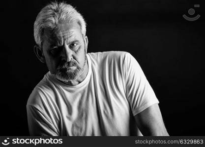 Portrait of a serious mature man looking at camera. Senior male with white hair and beard wearing casual clothes isolated on black background. Studio shot in black and white.