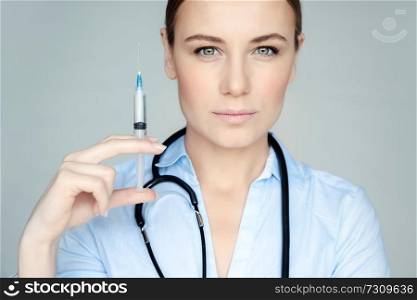 Portrait of a serious woman doctor with syringe isolated on gray background, doctor making anti aging treatment, injections of youth and beauty
