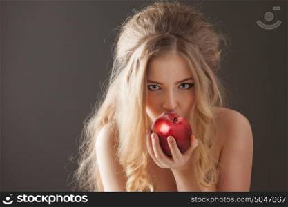 Portrait of a sexy beautiful nude pin-up girl from 60s or 70s, eating and biting a fresh red apple with temptation on dark background.