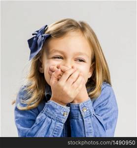 Portrait of a shy little girl covering mouth with her hands