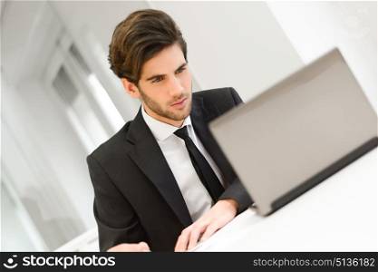 Portrait of a smiling businessman sitting at his laptop and working in his office