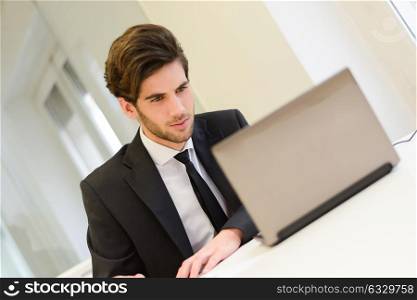 Portrait of a smiling businessman sitting at his laptop and working in his office
