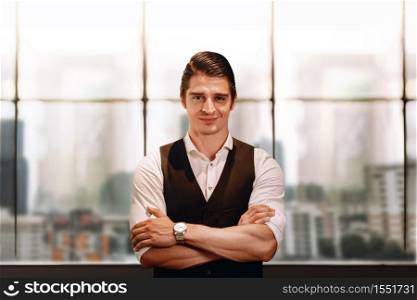 Portrait of a Smiling Caucasian Businessman, Crossed Arm and Look into the Camera. Blurred Office Building in the City as background